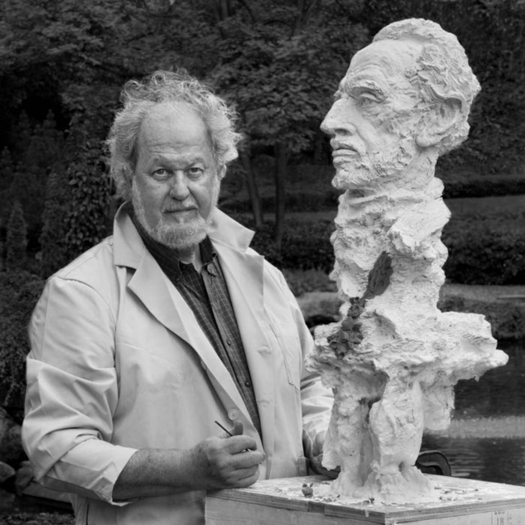 Produktfotografie Bonn zeigt einen Bildhauer mit Kunstwerk beim Fotoshooting im Park. Professioneller Produktfotograf für Werbeagenturen.
